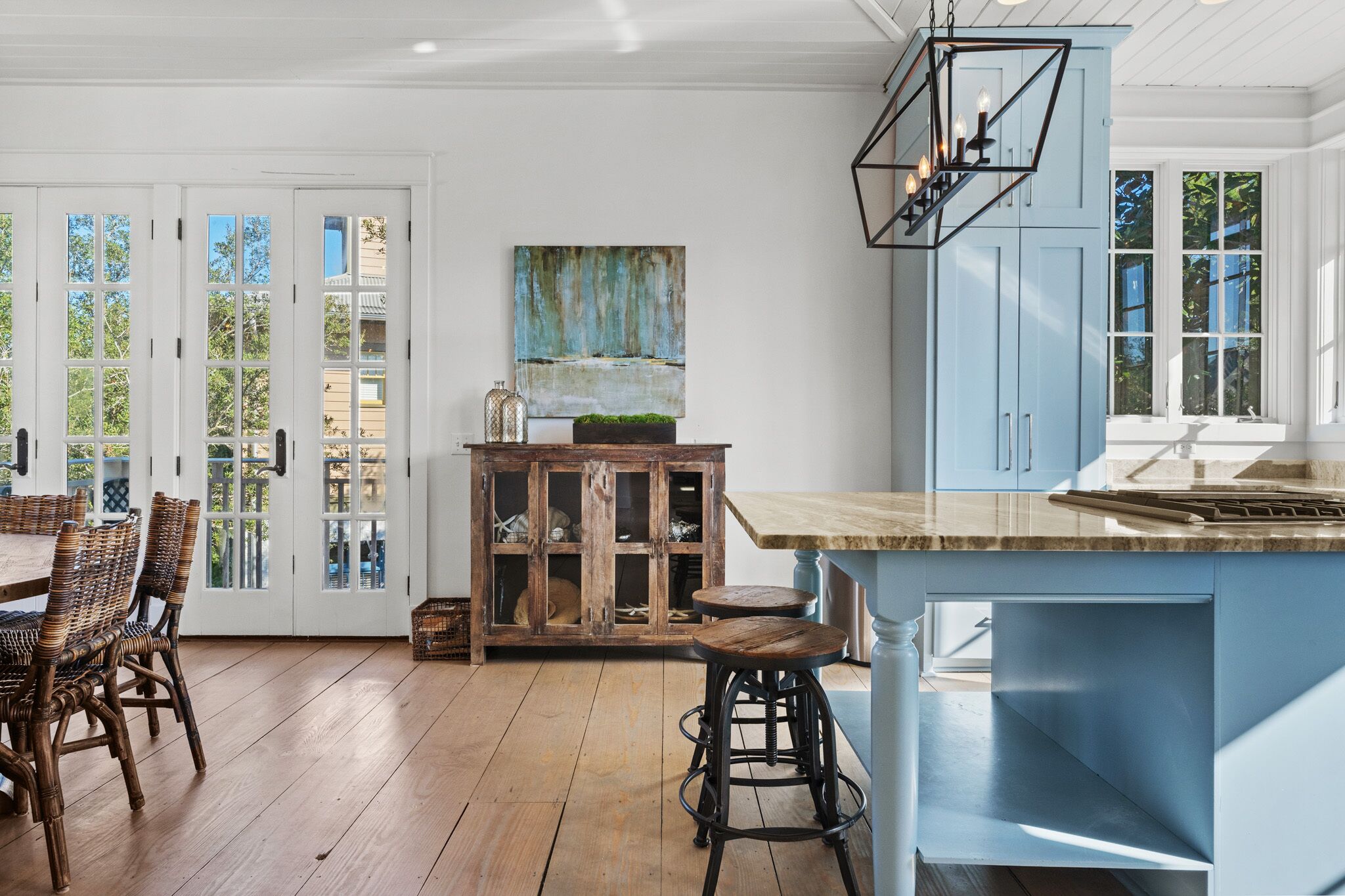 Une cuisine avec un îlot central bleu, des chaises en bois et un meuble avec des portes en verre.
