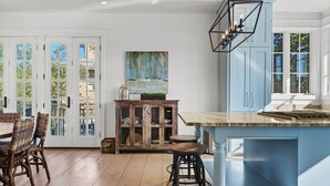 A kitchen with a blue island, wooden chairs, and a cabinet with glass doors. - Dejarnette Cottage w/Private Courtyard & Pool | 30A Rosemary Beach | My Beach Getaways (Rosemary Beach)