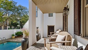 A poolside area with a wooden deck, lounge chairs, a large planter, and a door leading to a covered patio. - Dejarnette Cottage w/Private Courtyard & Pool | 30A Rosemary Beach | My Beach Getaways (Rosemary Beach)