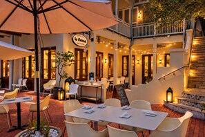 An outdoor seating area with tables and chairs, a sign for 'La Crema,' and a staircase leading to an upper level.