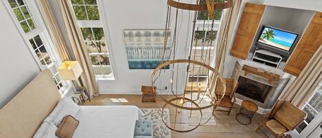 A spacious bedroom with a large bed, a hanging light fixture, a fireplace, and a television.