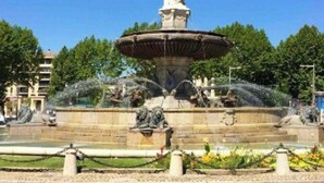 A public fountain with a statue in the center, surrounded by a stone basin and water features.