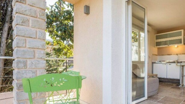 A balcony with a green metal chair, a stone wall, and a view of a kitchen area.