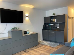 Una cocina moderna con televisor de pantalla plana, microondas integrado y hervidor en la encimera.