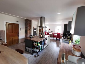 A modern kitchen with a central island, a dining area with red chairs, and a built-in stove. - Merlin - Our Celtic farm (Niederstetten)