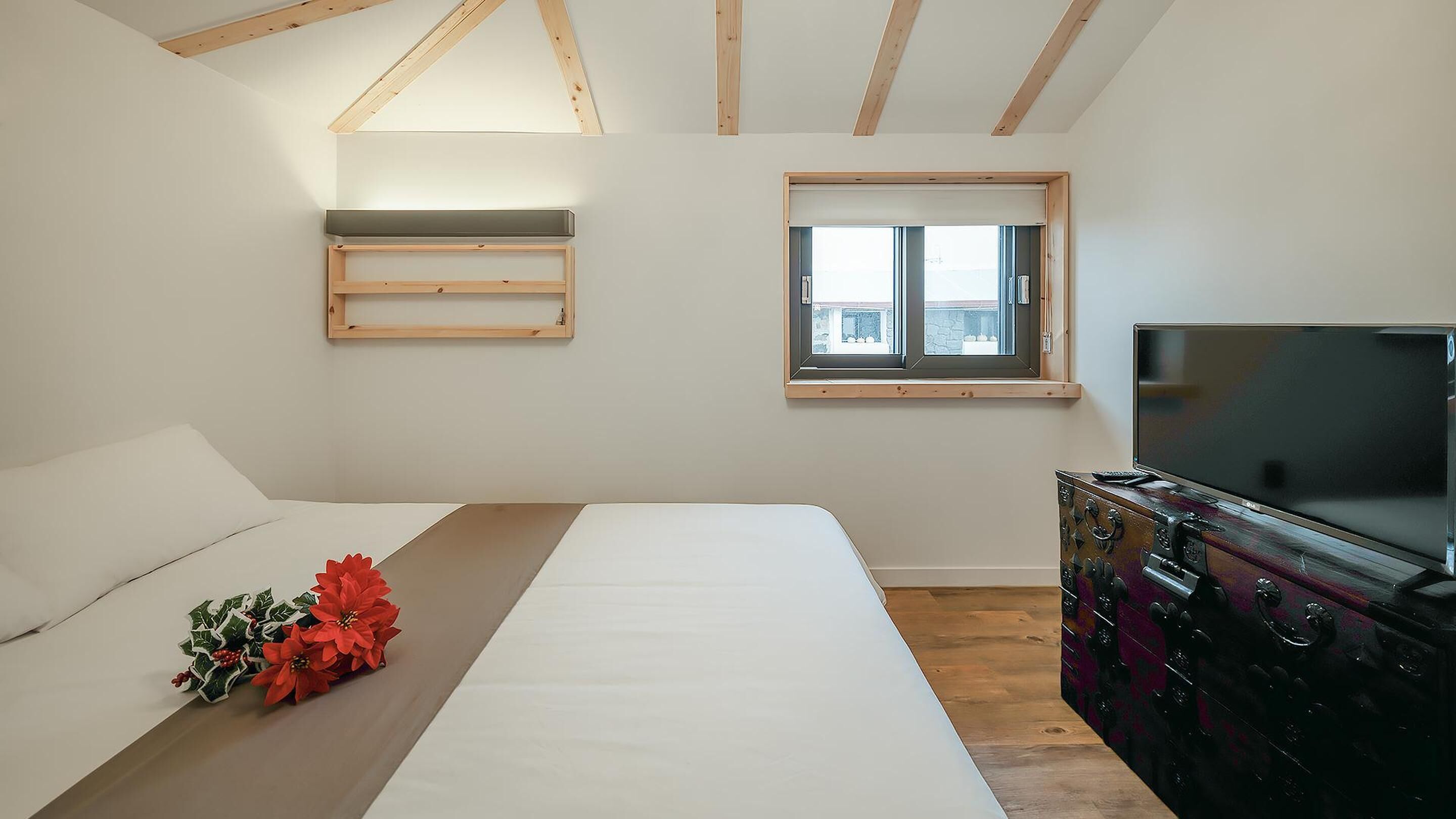 A bedroom with a bed, a dresser, a TV, a window, and a wooden ceiling.