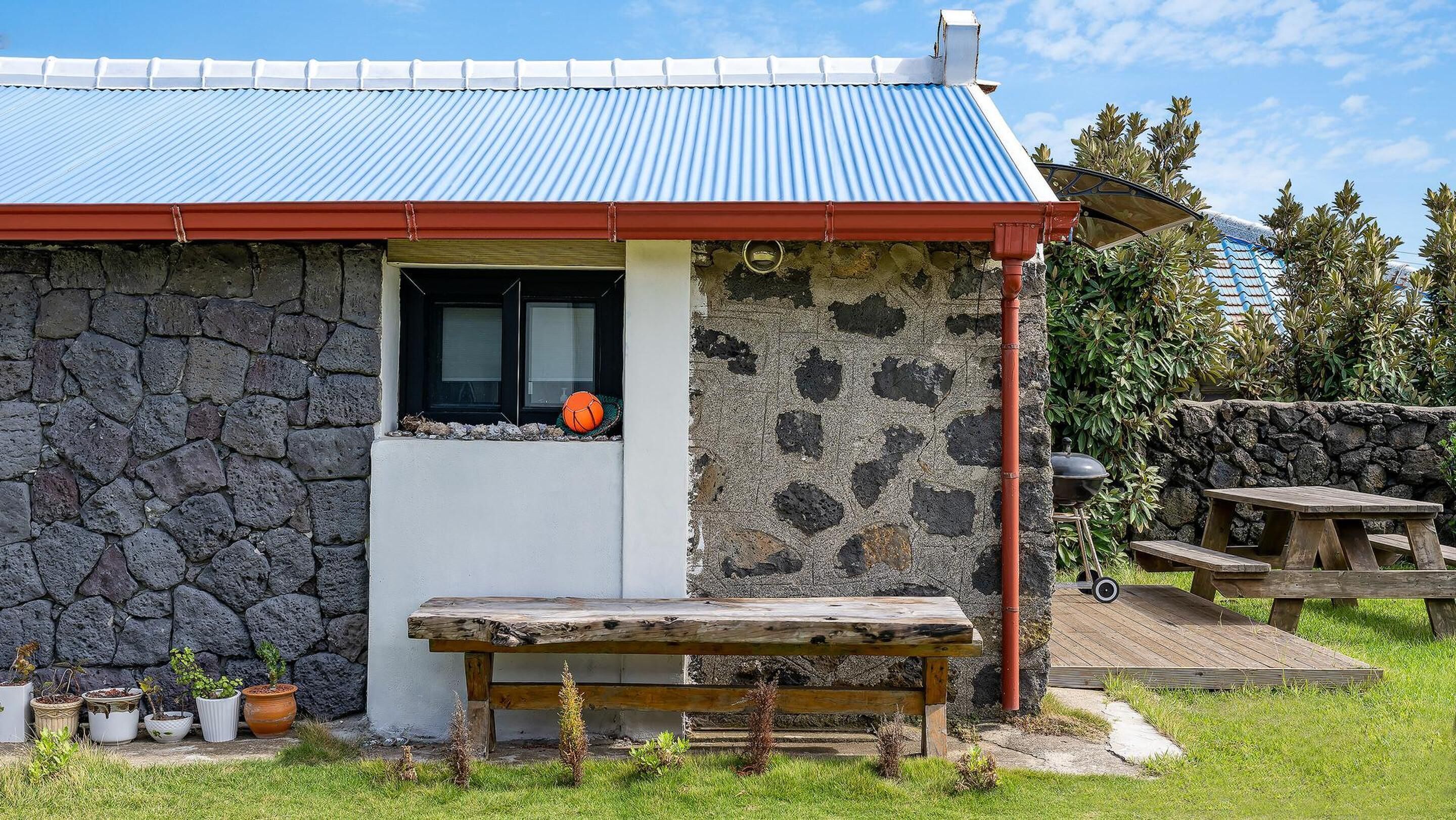 Un edificio in pietra con tetto in metallo, una panchina di legno e un tavolo da picnic.