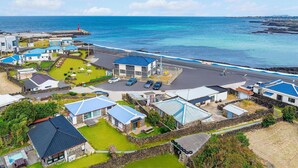 A coastal residential area with houses, a parking lot, and a view of the ocean. - Pyeongdae Moons Stay Pension (Jeju City)