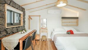 A cozy bedroom with a bed, a desk, and a chair. There's a stone wall, wooden beams, and a hanging light fixture. - Pyeongdae Moons Stay Pension (Jeju City)