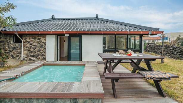 A house with a swimming pool, a patio with a table and chairs, and a stone wall. - Pyeongdae Moons Stay Pension (Jeju City)