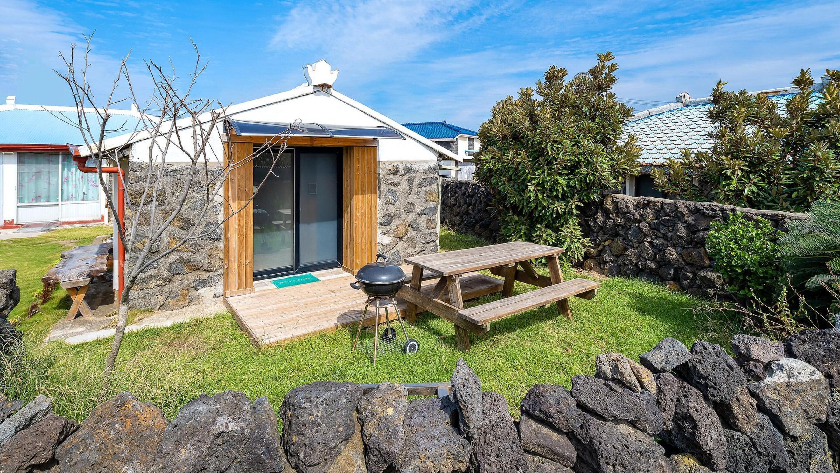 A small outdoor wooden structure with a sliding door, a picnic table, and a barbecue grill.