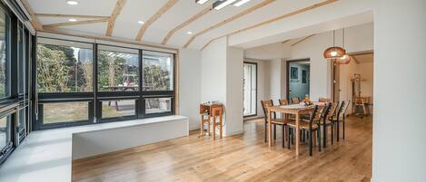A modern dining area with wooden flooring, a large window, and a dining table with chairs.