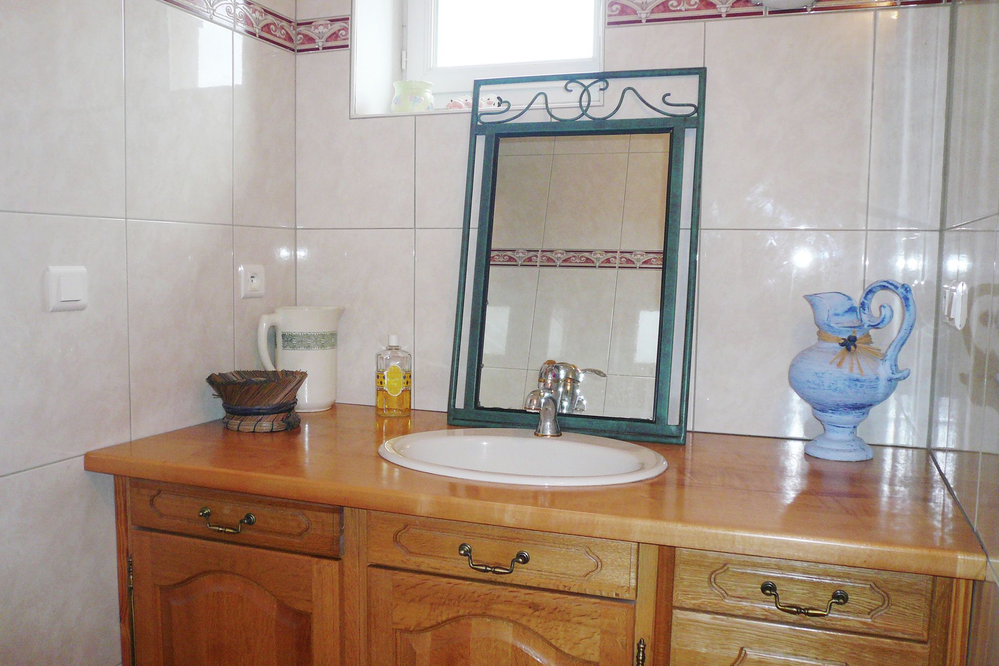 Un bagno con un mobile vanitario in legno, un lavandino bianco, uno specchio con cornice decorativa e un vaso blu sul ripiano.