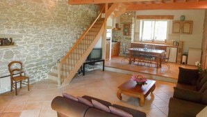 A spacious living area with a stone wall, wooden staircase, a dining area with a table and chairs, and a kitchen in the background. - Villa in Conilhac with Private Terrace (Conilhac-De-La-Montagne)
