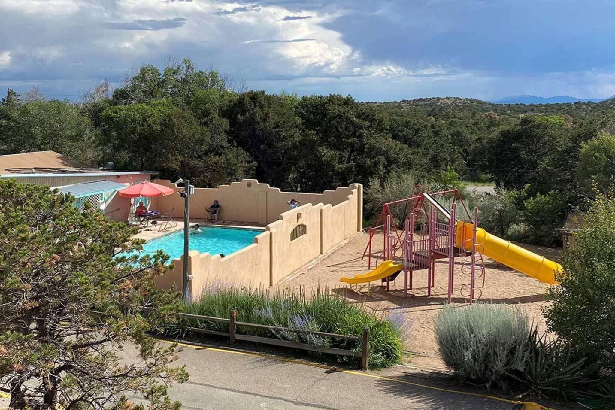 A pool area with a slide and a person swimming, surrounded by trees and hills.