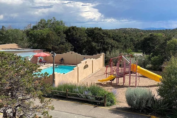 A pool area with a slide and a person swimming, surrounded by trees and hills.
