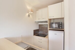A compact kitchen with a built-in microwave, a small refrigerator, and a stove. - Sunny Stay in Lavender Land (BONNIEUX)