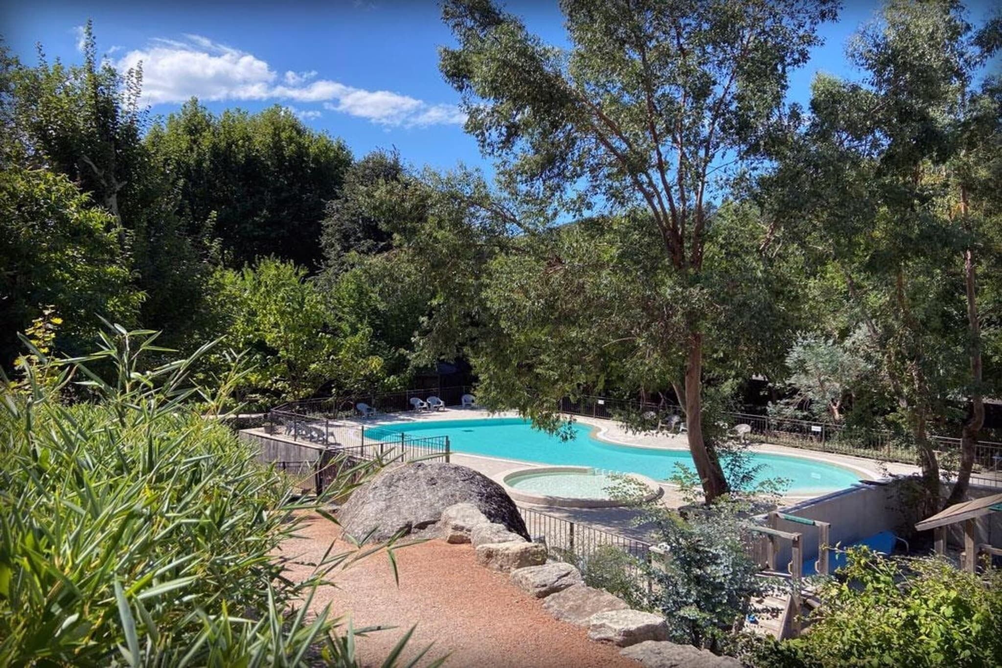 Une piscine entourée d’arbres et bordée d’une zone rocheuse.