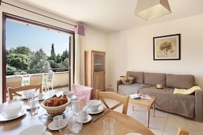 A dining area with a table set for breakfast, a sofa, and a balcony with a view of trees.