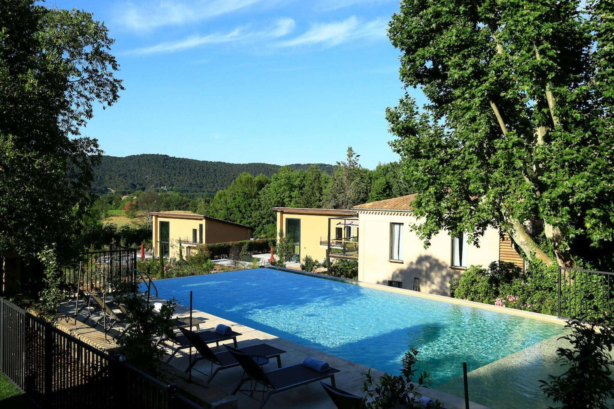 A swimming pool with lounge chairs and a view of two buildings in a natural setting.