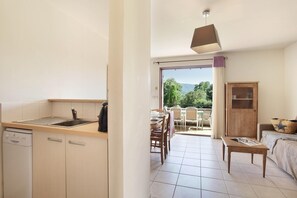 A compact kitchen with a dishwasher, a coffee maker, and a dining area with a table and chairs. - Sunny Stay in Lavender Land (BONNIEUX)