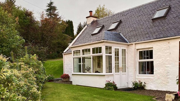 A white house with a sloped roof, large windows, and a well-maintained lawn.