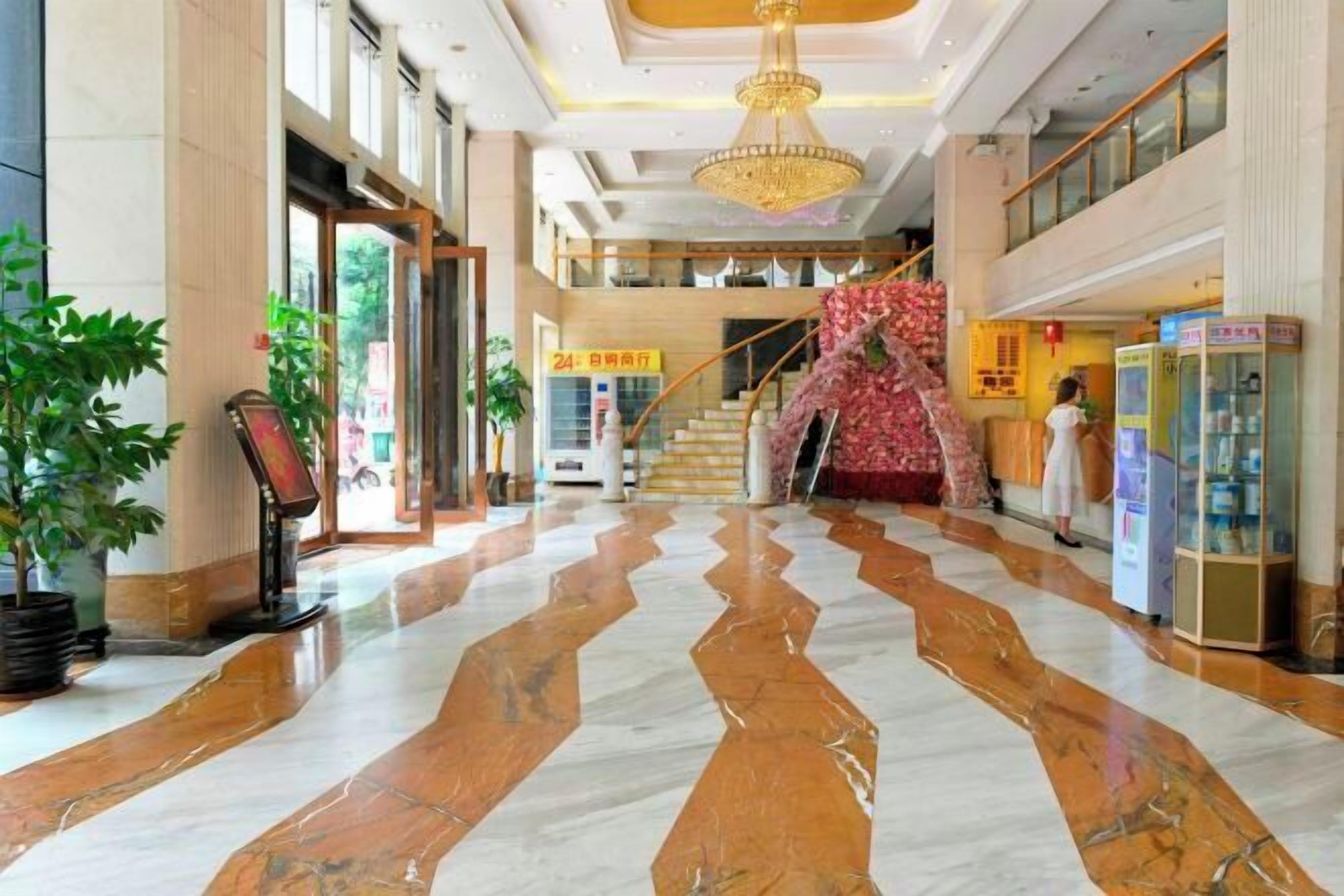 A spacious lobby with a marble floor, a chandelier, and a staircase leading to an upper level.