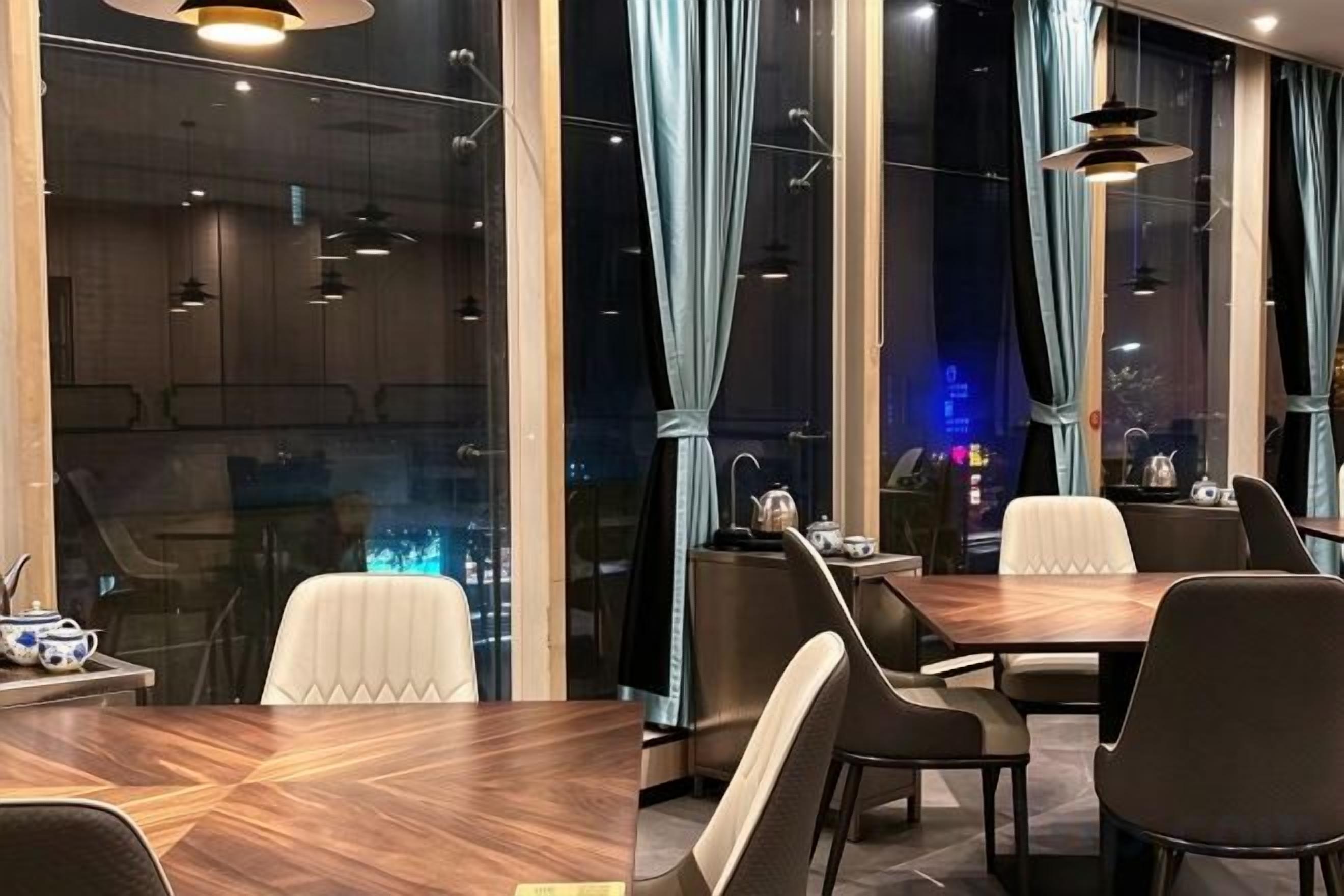 A modern dining area with a wooden table and chairs, large windows with curtains, and pendant lighting.