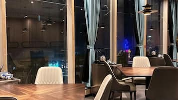 A modern dining area with a wooden table and chairs, large windows with curtains, and pendant lighting.