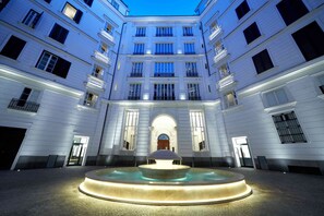 Un cortile centrale con una fontana, circondato da edifici a più piani con balconi e ampie finestre.