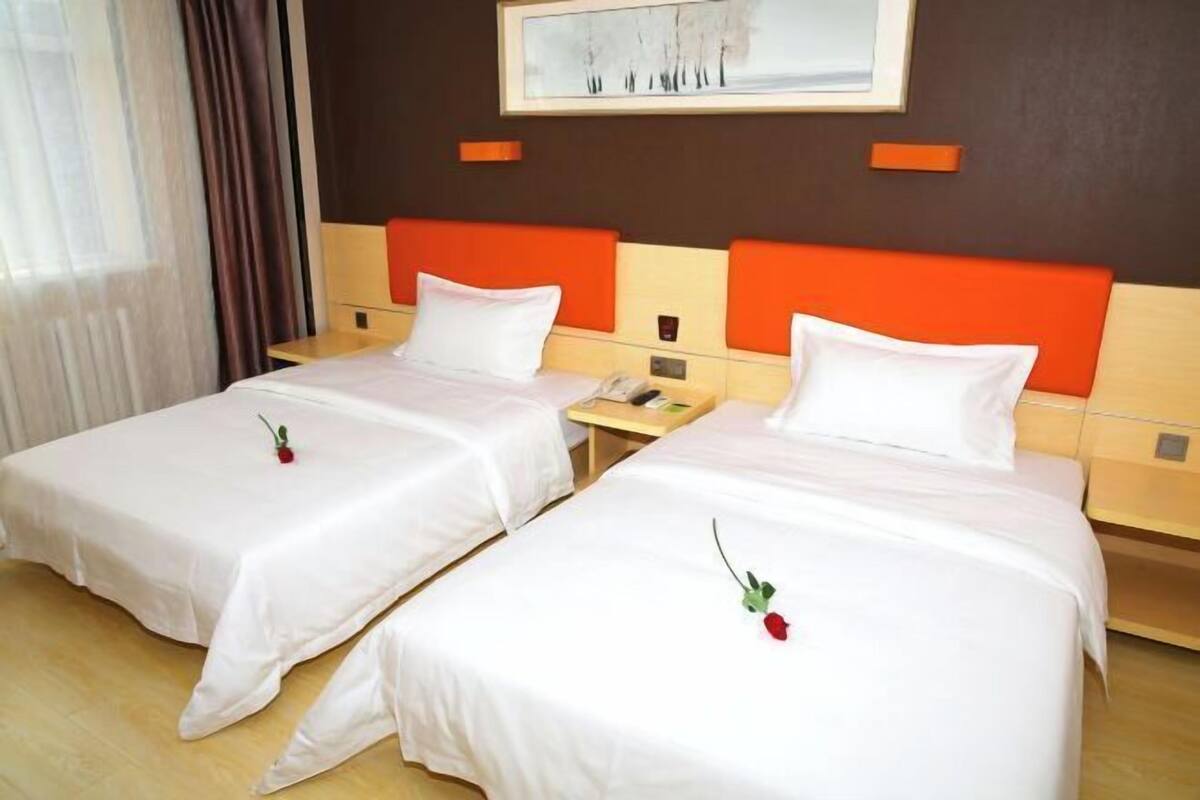 A hotel room with two beds, each with white bedding and a single red rose.