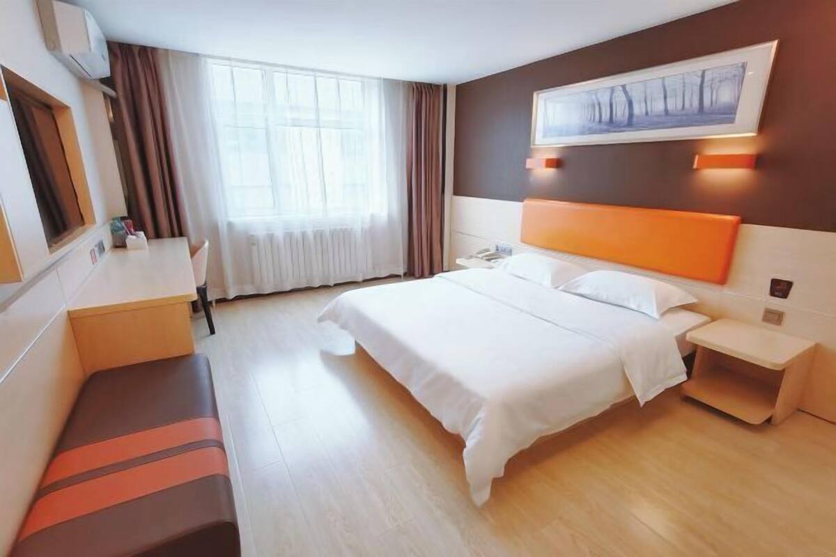 A hotel room with a bed, bedside tables, a desk, a bench, and a window with curtains.