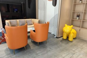 A modern interior with a sofa and two orange chairs, a yellow bear sculpture, and a wooden shelving unit.
