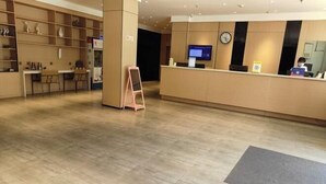 Un espace d’accueil d’hôtel comprenant un comptoir, un téléviseur et une horloge.