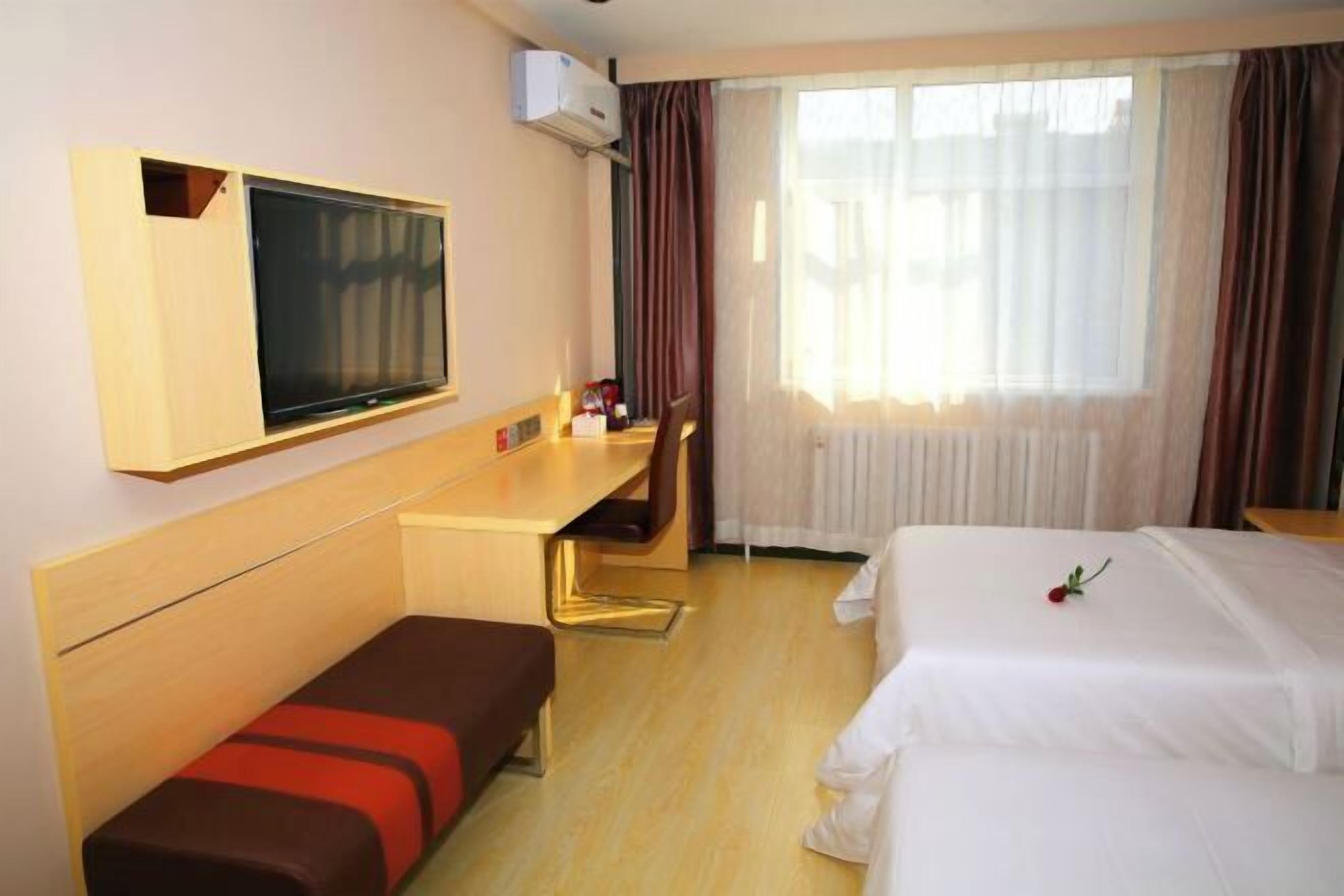 A hotel room with a bed, a desk, a TV, and a window with curtains.