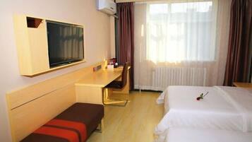 A hotel room with a bed, a desk, a TV, and a window with curtains.