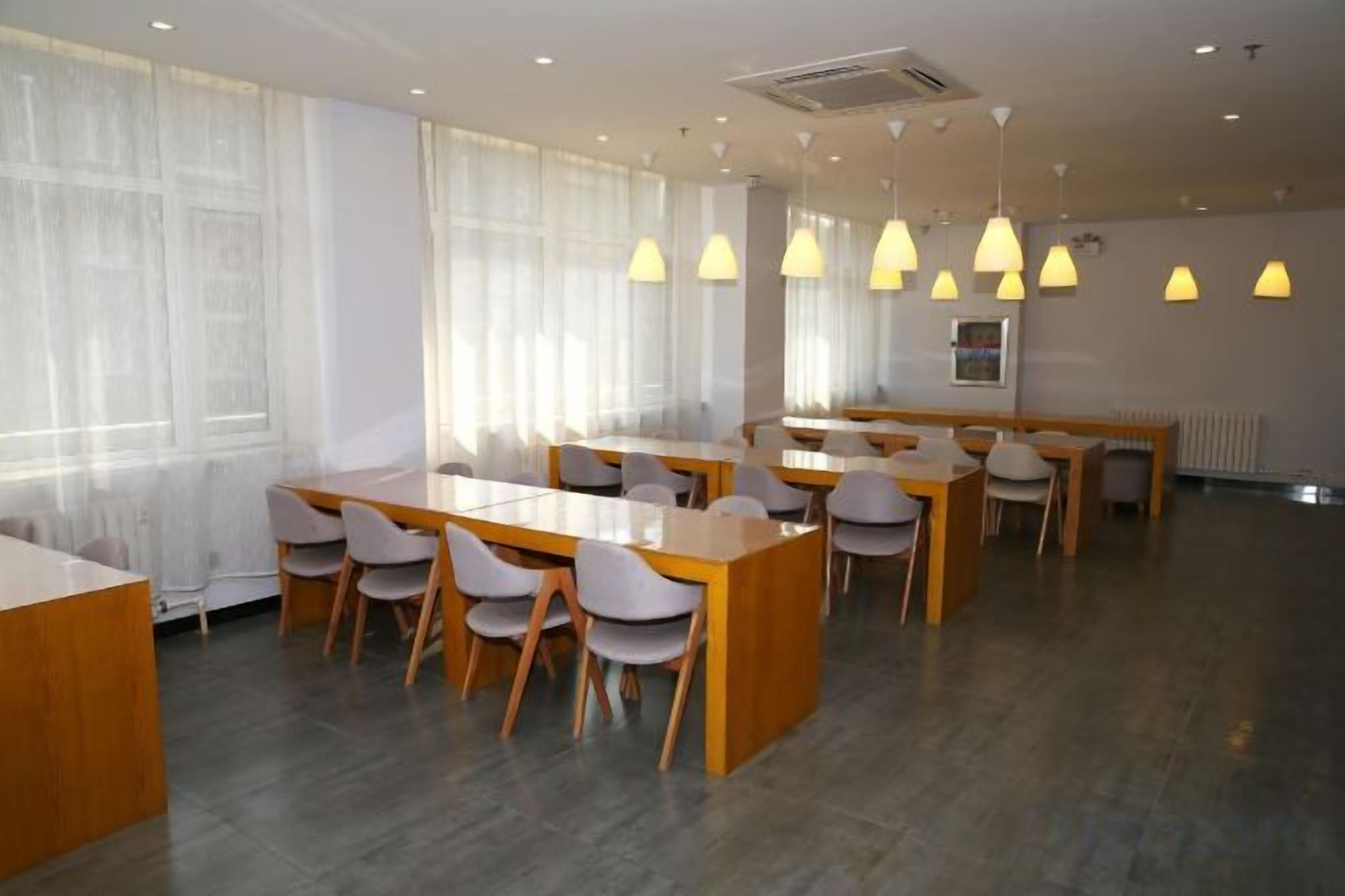 Un comedor amplio con varias mesas y sillas, ventanas grandes con cortinas translúcidas e iluminación colgante.