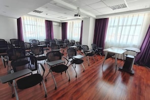 Une salle de conférence avec des rangées de chaises, un projecteur et une table.