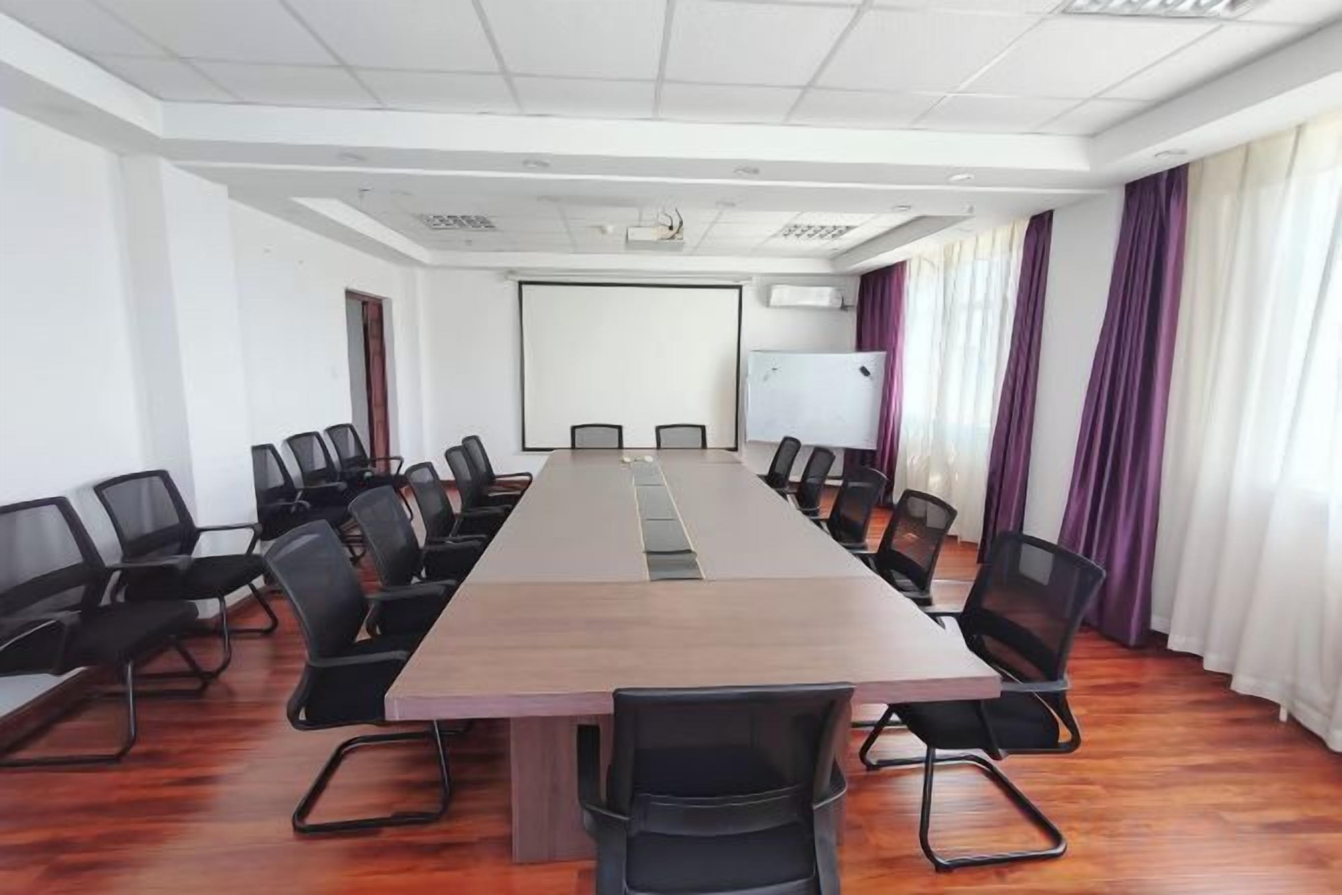 Un salón de conferencias con una larga mesa, sillas, una pantalla de proyector y una pizarra.