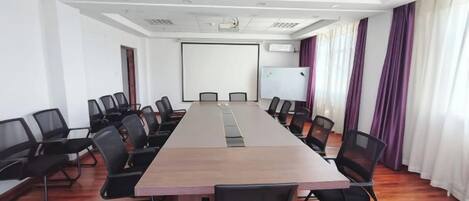 Un salón de conferencias con una larga mesa, sillas, una pantalla de proyector y una pizarra.