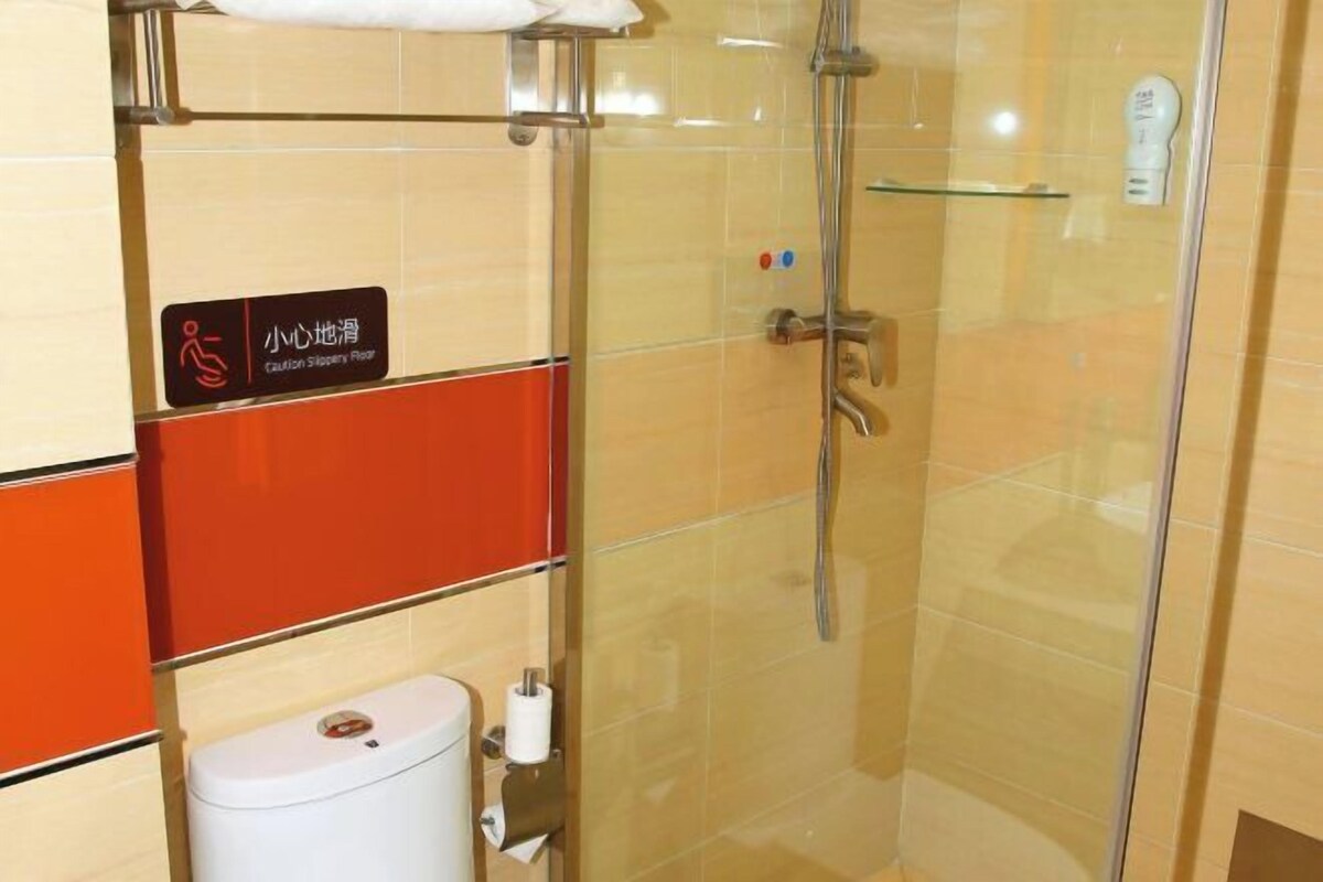 A bathroom with a caution sign, a toilet, a glass shower enclosure, and a soap dispenser.
