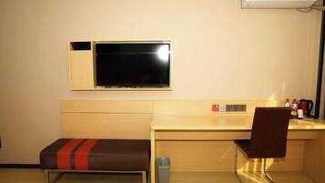 A hotel room with a bed, a desk, a chair, a TV, a trash bin, and a heater.