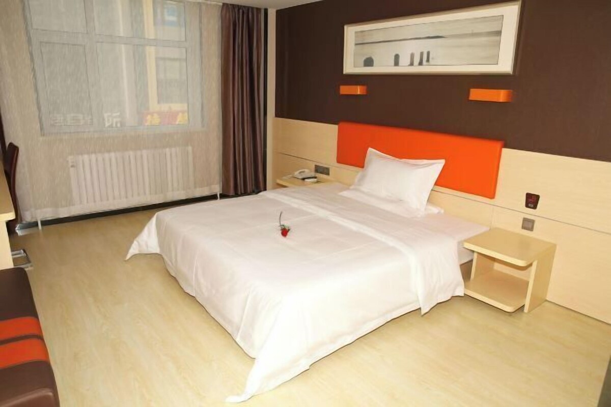 A hotel room with a bed, bedside table, and a window with curtains.