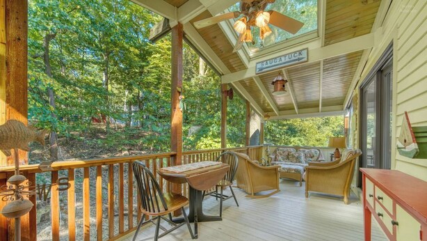 A covered porch with a wooden railing, a table, chairs, and a sofa.