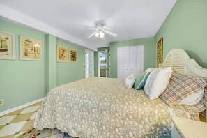 A bedroom with a bed, a ceiling fan, and framed artwork on the walls.