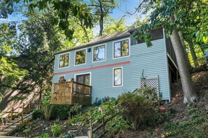 A two-story house with a wooden deck, surrounded by trees and a garden.