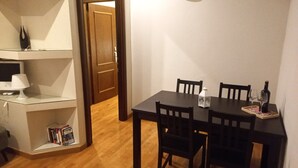 A dining area with a wooden table, four chairs, a white table lamp, a wine bottle, and a wine glass on a tray. - Stefano House Apartment Trevi Fountain  (Roma)