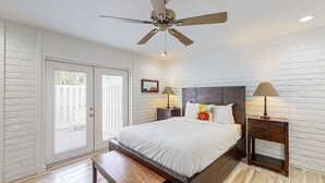 Un dormitorio con cama, dos mesitas de noche, un ventilador de techo y un banco de madera.