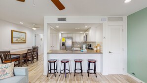 Una cocina moderna con armarios blancos, un refrigerador de acero inoxidable y una barra con taburetes.