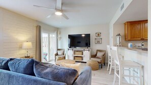 A living room with a sofa, TV, and dining area with chairs and a kitchen counter.